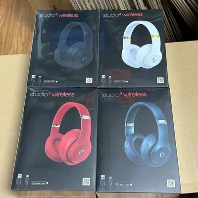 Four boxed Beats Studio3 over-ear headphones in black, white, pink and blue, standing upright on a wooden floor.