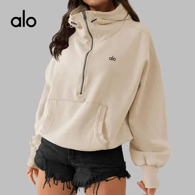 A cream half-zip sweatshirt worn by a model cropped above the chin, with a small alo wordmark in the top corner of the frame.