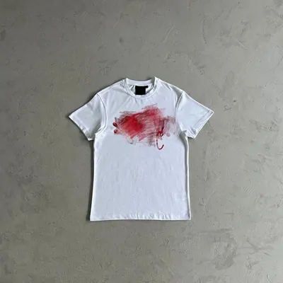 A white T-shirt laid flat on gray concrete, with a red abstract print across the chest.