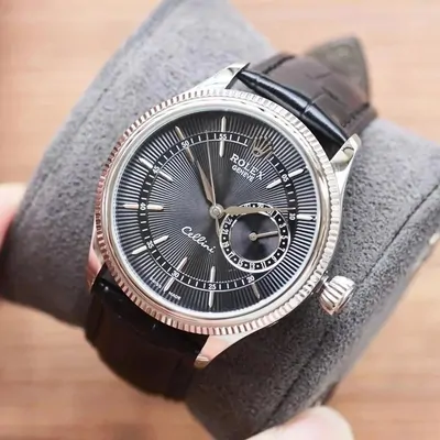 A Rolex Cellini with a black dial and a leather strap, worn on a wrist against a gray sleeve.